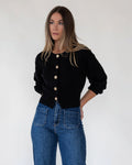 Gold buttons running down the front of a cropped black knit cardigan