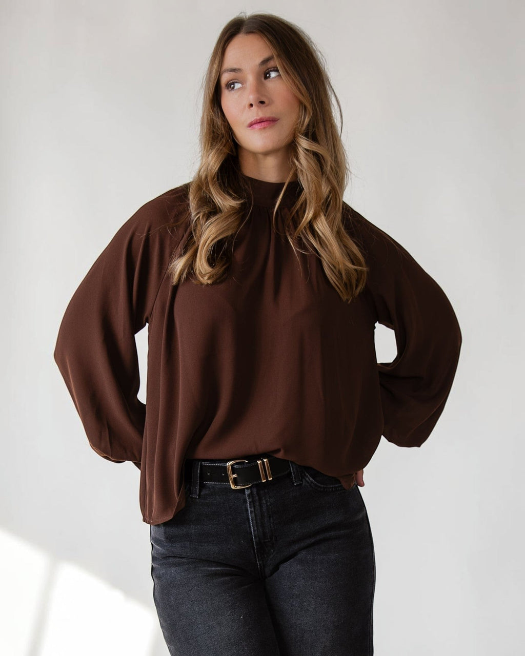 Gathered mock neckline giving quiet structure to a brown woven top