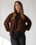 Gathered mock neckline giving quiet structure to a brown woven top