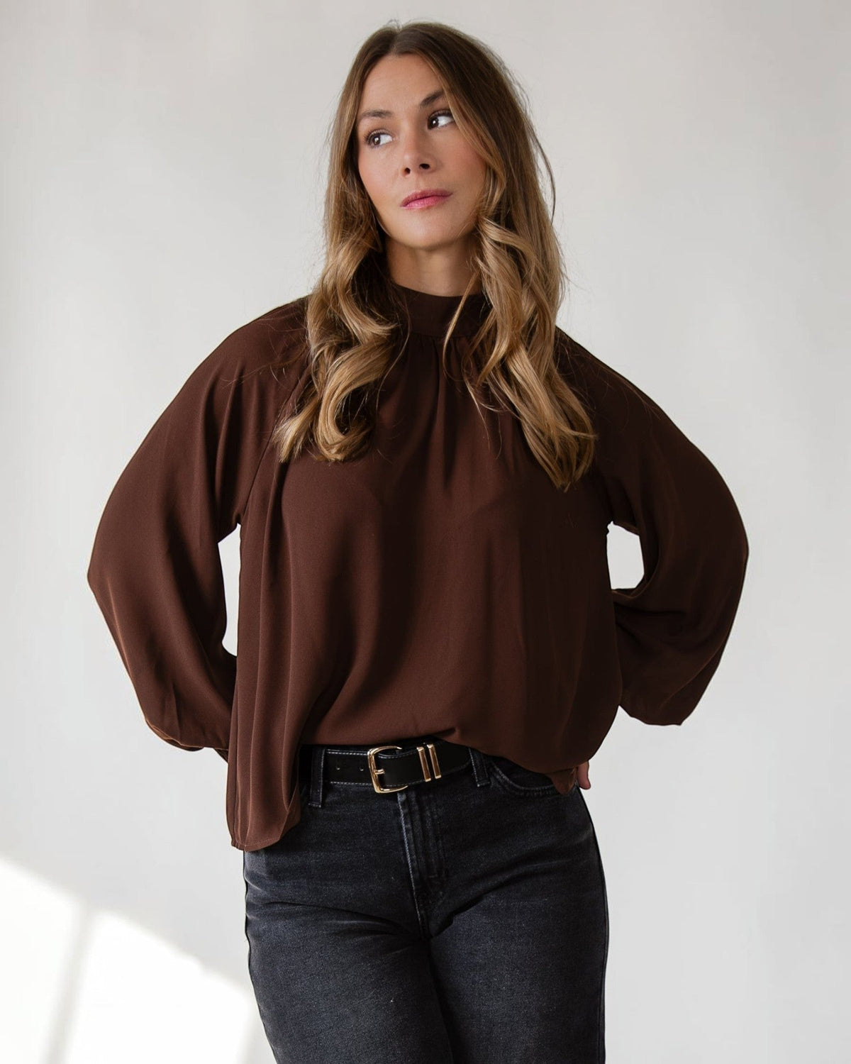 Gathered mock neckline giving quiet structure to a brown woven top