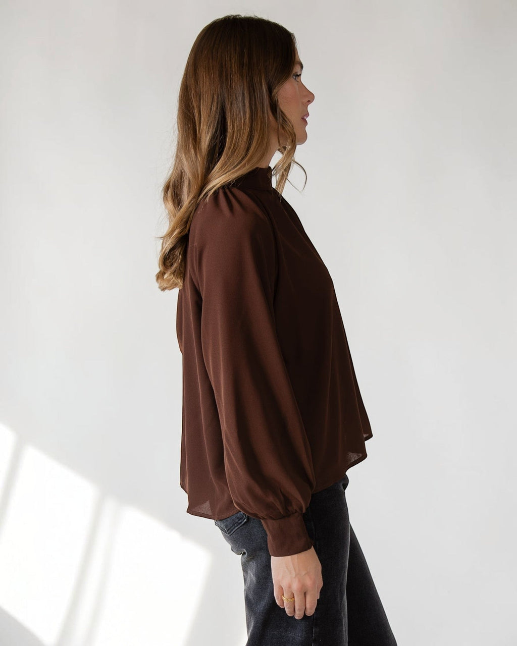 Button keyhole closure at the back neck of a brown mock neck top