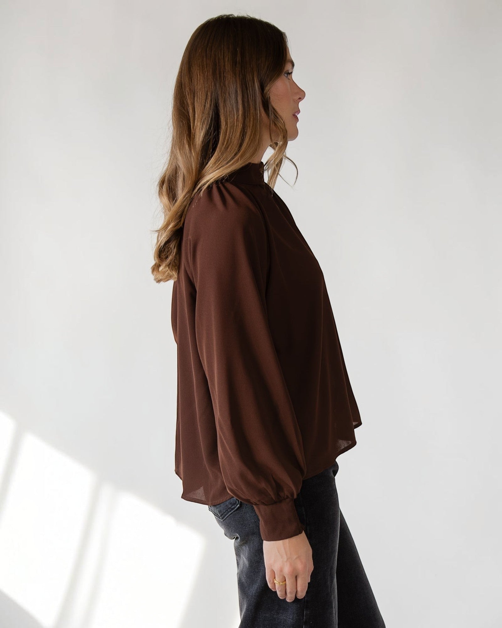 Button keyhole closure at the back neck of a brown mock neck top